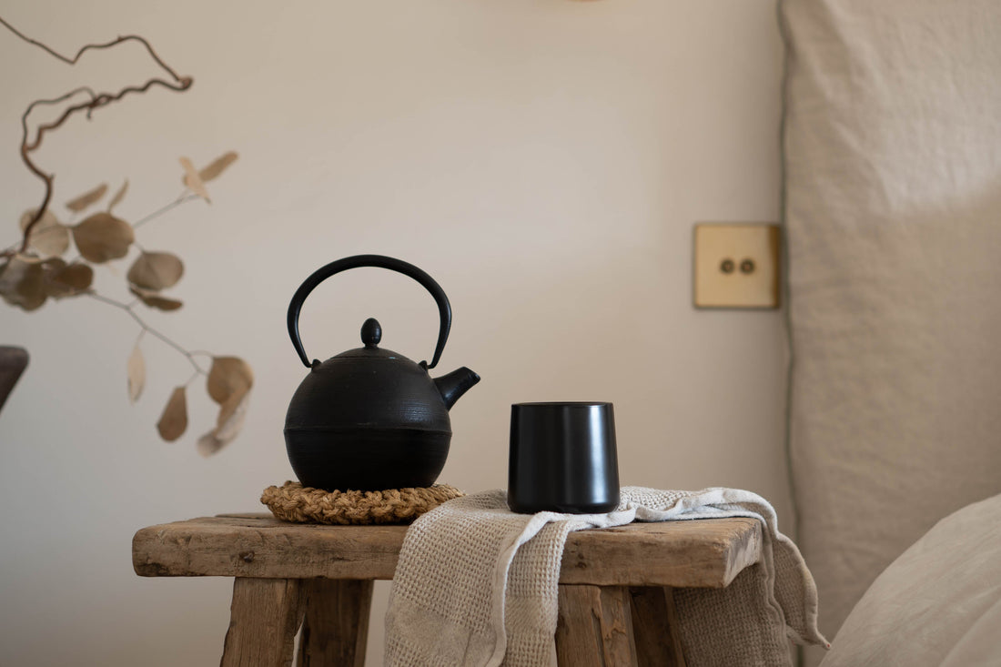 Black tea kettle and handleless cup sit on a wooden bench